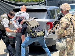 Police officers detain a person next to a member of the National Guard at a location given as Los Angeles, California, in this handout from ICE.